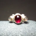 geschwungener, barock anmutender Granatring mit einen tiefrotem Granatcabochon und zwei Labradorithen in Rosecut Schliff, gefasst in 750er Roségold